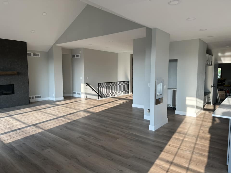 Finished open-plan living room with dark tile fireplace wall, vaulted ceiling, and open staircase with decorative iron railing
